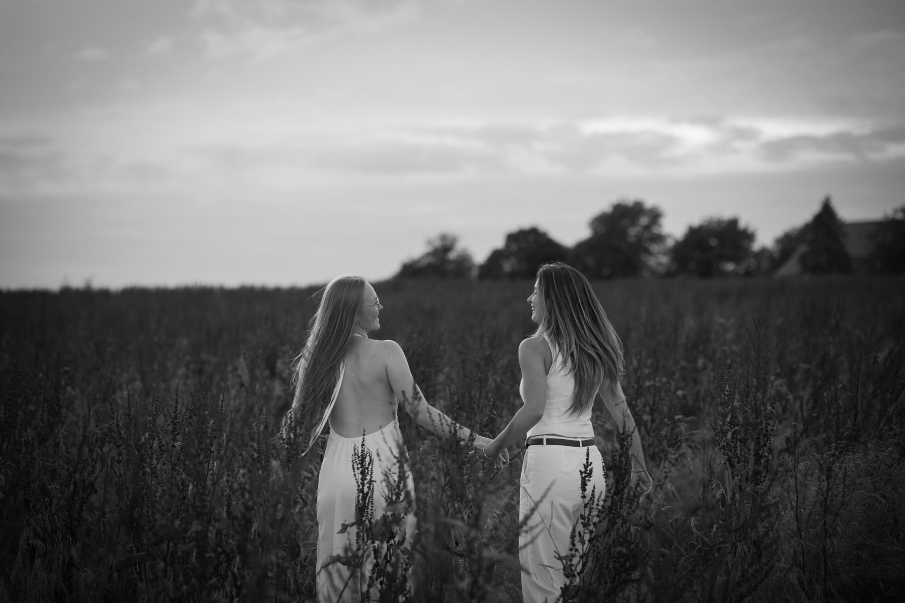 Zwei Frauen gehen Hand in Hand durch ein Feld, Schwarzweißfoto