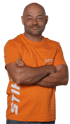 Glücklicher Mann mit Glatze und Bart, der ein orangefarbenes "STIHL" T-Shirt trägt und die Arme verschränkt hat.