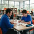 A teacher in a blue shirt helps a teenage student study a textbook at a desk in a bright classroom or library.
