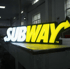 Leuchtendes Subway-Logo mit "SUB" in Weiß und "WAY" in Gelb, das Y als Pfeil geformt.