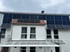 Gebäude mit großen Solarmodulen auf dem Dach und einer kleineren Gruppe auf einem Vorsprung.