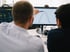 Zwei Männer betrachten einen Computermonitor mit einer Graphenanalyse und zeigen mit einem Stift auf die Kurven.