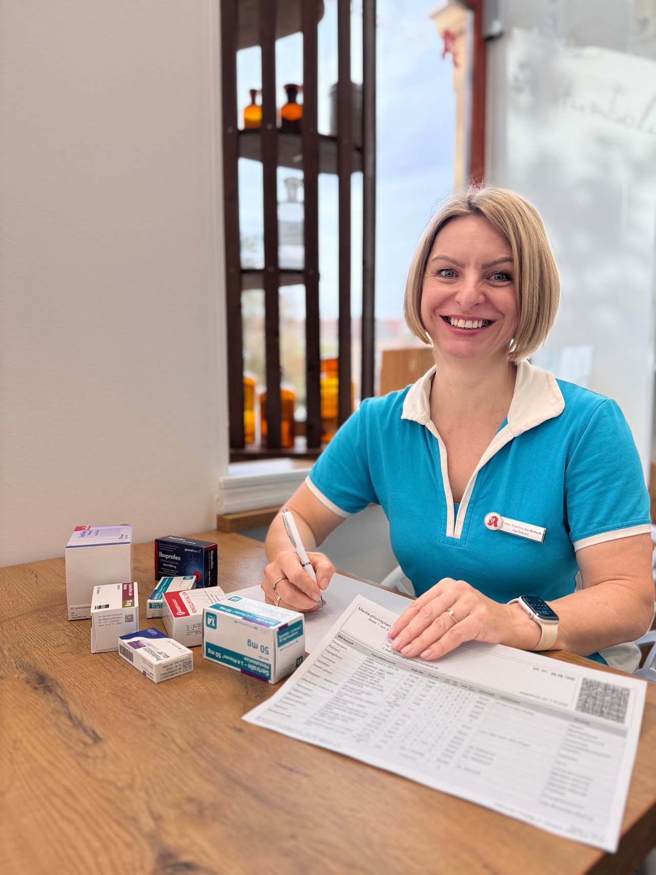 Apothekerin Celina Zakrzewska-Hadasik am Beratungstisch mit Medikationsplan und Arzneimittelpackungen