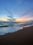 Ocean waves wash onto a dark sandy beach under a colorful sunset sky.