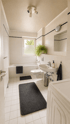 Modernes Badezimmer mit hellen Fliesen, Badewanne, Waschbecken, WC und dunkelgrauen Badematten.