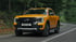 Ein orangefarbener Ford Ranger Pickup-Truck fährt auf einer kurvigen Straße durch einen Wald.