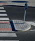 A semi-circular concrete traffic island with a metal pole stands in the middle of a pedestrian crosswalk.
