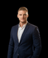 Mann im dunkelblauen Anzug und weißem Hemd, blickt direkt in die Kamera.