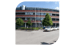 Ein modernes Gebäude mit brauner Fassade, davor parken weiße Autos auf einer Straße.