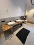 Badezimmer mit zwei ovalen Waschbecken auf einer Holzwerkbank, schwarzem Teppich und Toilette Reutte