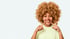 Eine lächelnde Frau mit blonden Locken zeigt mit beiden Zeigefingern auf ihre Zähne.
