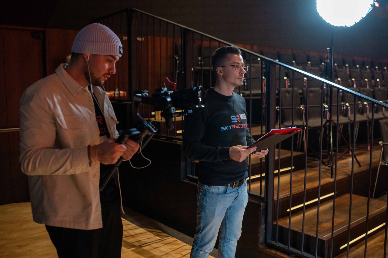 Zwei Mitarbeiter von Skyrecords filmen mit Kamera und Klemmbrett in einem Veranstaltungssaal