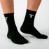 Zwei Füße tragen schwarze Socken mit weißem „T“-Logo.