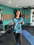 Lachende Frau in Sportkleidung zeigt im Fitnessstudio beide Daumen hoch.