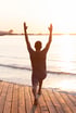 A person with raised arms standing on a beach at sunset.