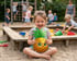 Kleines Mädchen sitzt im Sandkasten und hält ein aufblasbares Ananas-Spielzeug.
