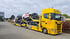 Gelber ADAC Autotransporter-LKW mit vier schwarzen und einem weißen STRABAG-Auto auf der Ladefläche.