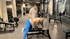 Ein Trainer hilft einem Mann beim Rudern mit einer Hantel auf einer Bank in einem Fitnessstudio.