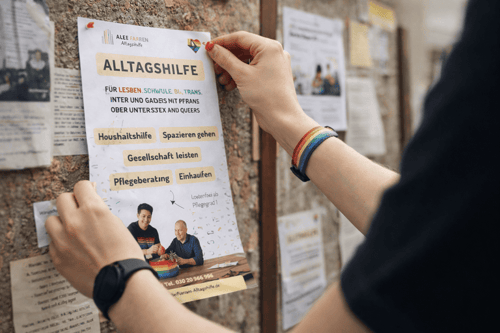 Hands pin an “ALLTAGSHILFE” poster to a notice board.