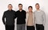 Vier Männer mit dunklen Hemden stehen vor einem weißen Hintergrund und lächeln.