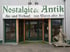 Antikgeschäft Nostalgie & Antik in Scheifling – Ladenfront mit grüner Beschriftung, Eingang mit Glasfront und antiken Möbeln im Innenbereich
