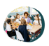 Fünf Kinder sitzen gemeinsam an einem Schultisch und essen gesundes Pausenbrot und Obst in einem hellen Klassenzimmer.