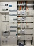 Elektrischer Verteilerkasten mit Sicherungen, Zähler und Patchpanels mit orangefarbenen Kabeln.