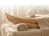 Barfuß liegende Beine auf einer Massageliege mit einem zusammengerollten Handtuch unter den Knöcheln in Spa-Atmosphäre.