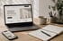 Laptop und Smartphone zeigen "Webdesign, das dein Business nach vorne bringt" auf einem Schreibtisch mit Notizbuch und Tasse.