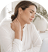 A woman in a white blouse closes her eyes and massages her neck to relieve pain.
