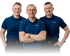 Drei lächelnde Männer in blauen Poloshirts, der mittlere Mann hat die Arme verschränkt.
