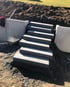 Blockstufen aus grauem Beton bilden eine Außentreppe an einem Erdhang zwischen L-Steinen auf einer Baustelle.
