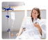 Woman in a white robe holding a glass of water, sitting beside an IV drip stand.