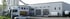 Weiße Lagerhalle mit LKW SIC-Beschriftung, Garagentoren, geparkten LKWs und einem Lieferwagen.