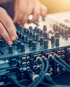 Hände eines DJs an einem Mischpult mit vielen Knöpfen und Kabeln.