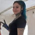 Junge Frau mit blauen Haaren, Tattoos und schwarzen Ohrtunneln macht ein Friedenszeichen.