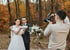 Photographe prenant des photos d'un couple de mariés avec un petit gâteau et un bouquet dans un décor forestier d'automne.