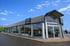 Modernes Mazda-Autohaus mit großen Glasfenstern, dahinter ausgestellte Autos, und dem Mazda-Logo über dem Eingang.