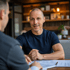 Excel Beratung im Dialog: Excel-Experte bespricht Prozessoptimierung mit Kunde, prüft Unterlagen in moderner Lounge.