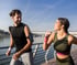 A happy couple jogging outdoors by the water on a sunny day