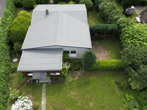 Draufsicht auf ein graues Haus mit Garten, Rasenflächen, Büschen und Bäumen.