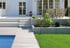 Weiße Terrasse mit Treppe, Holzsteg zum Pool, Garten mit Rasen und Hochbeet.