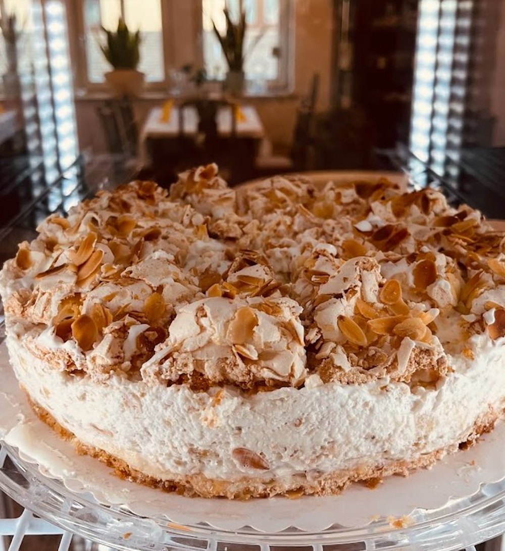 Sahnetorte mit knusprigem Baiser und gerösteten Mandelblättchen auf einer Glasplatte