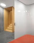Eine moderne Treppe aus hellem Holz führt nach oben, daneben eine weiße Wand und ein orangefarbener Teppich.