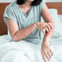 Person in gray shirt with red, irritated arms, scratching skin on a white bed