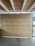Carport mit einer Sichtschutzwand aus horizontalen Holzlamellen unter weißen Dachbalken auf grauem Pflastersteinboden.