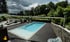 Ein rechteckiger Pool mit blauer Wasseroberfläche, umgeben von dunklem Holzdeck und üppigem Grün.