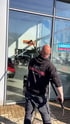 Ein Mann in schwarzem Hoodie mit der Aufschrift „AMC GLASREINIGUNG“ reinigt ein großes Fenster mit einem langen Teleskopwischer.