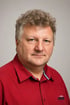 Mann mittleren Alters mit lockigem grauem Haar und rotem Hemd blickt in die Kamera.