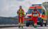 Zwei Rettungsschwimmer in roten und gelben Uniformen gehen vor einem DLRG-Lingen-Rettungswagen auf einer Brücke.